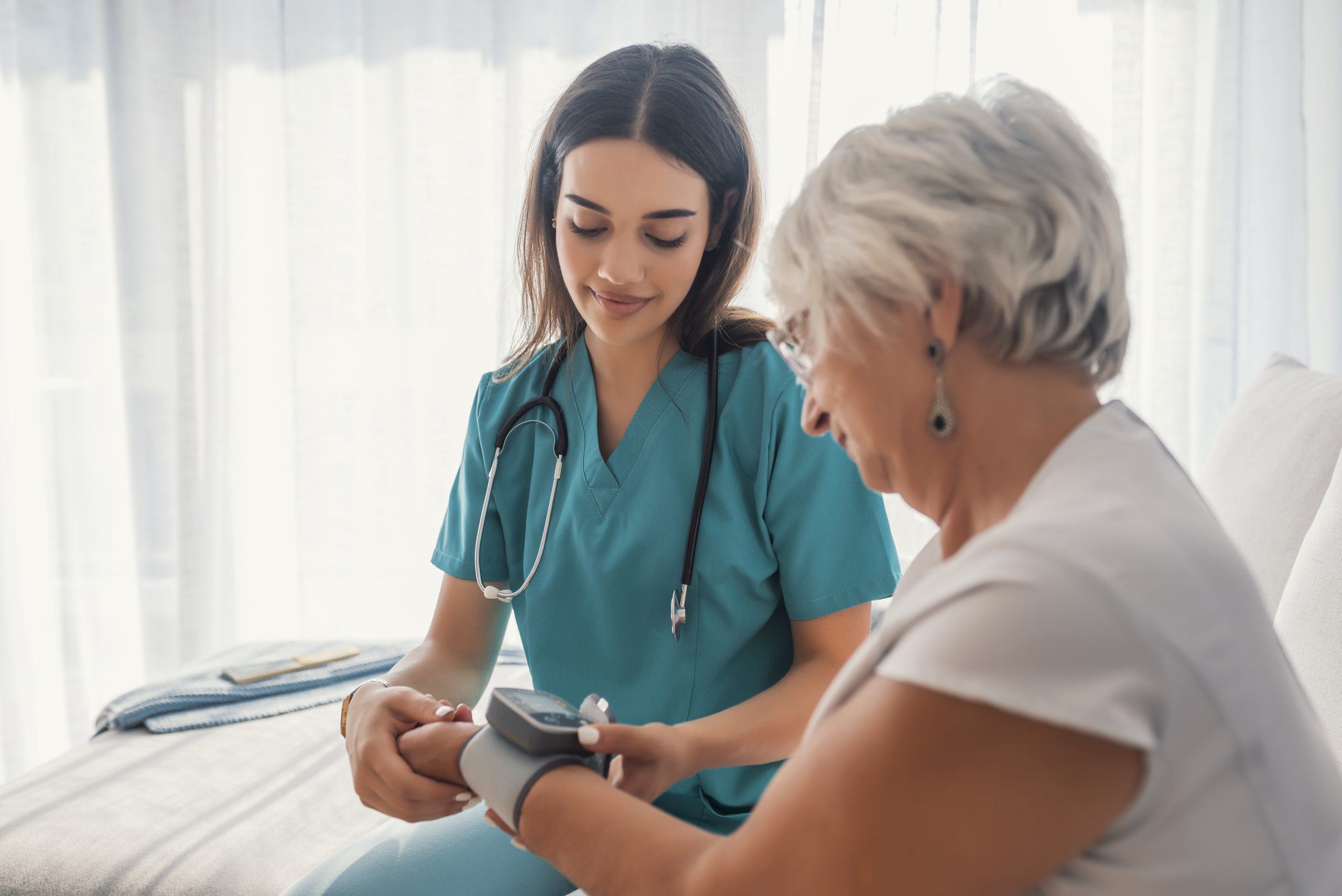 Young nurse measuring blood pressure of elderly woman at home. Female nurse checking blood pressure of a senior woman at home,Home carer checking patients blood pressure